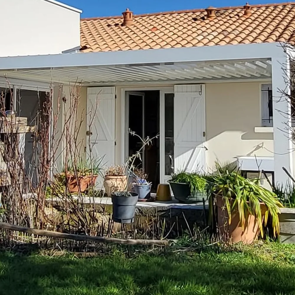 Pergola bioclimatique blanche adossée à une maison avec terrasse